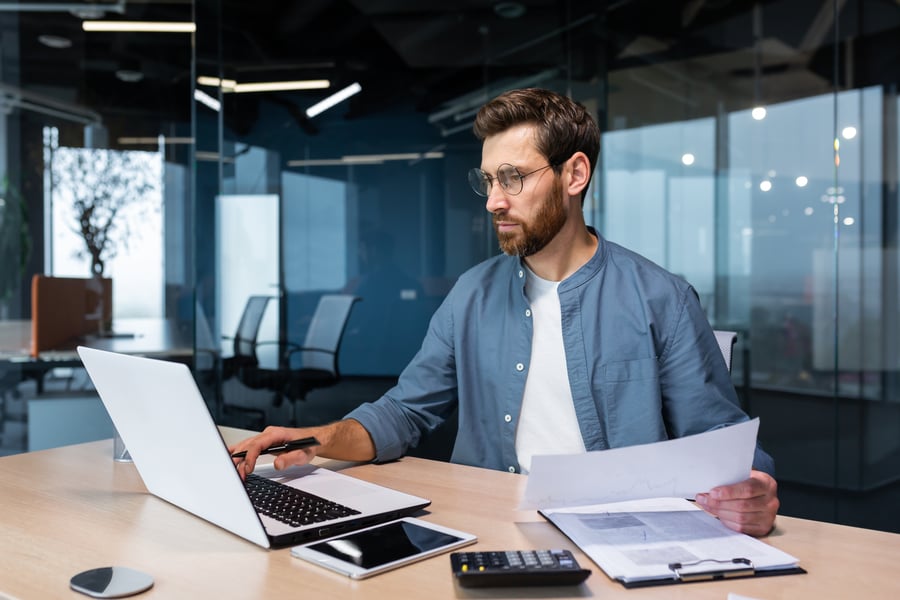 Man looking at computer and stack of papers